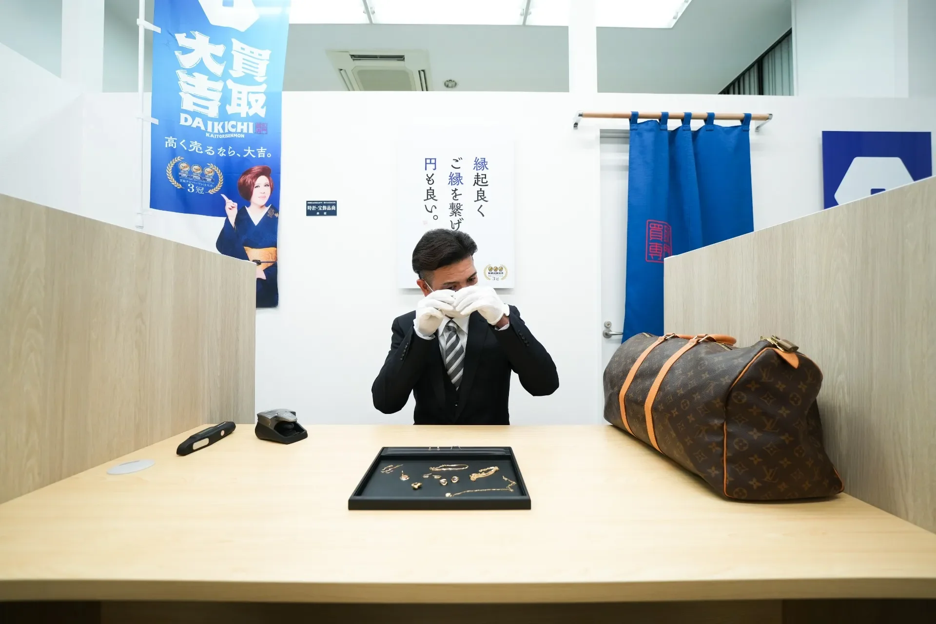 買取店のカウンターで腕時計とアクセサリーを前に査定を受ける手元
